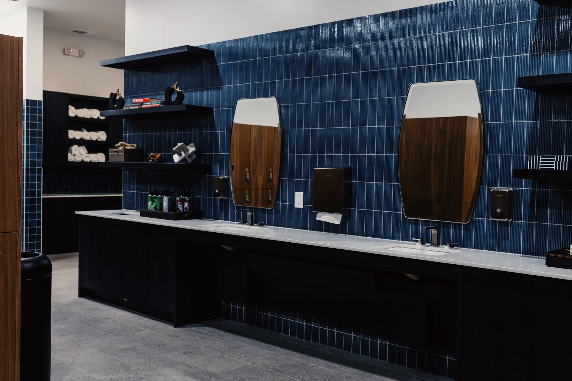 The men's locker room at THIS Gym — navy tile, grooming stations, and private showers — image 1 of 3