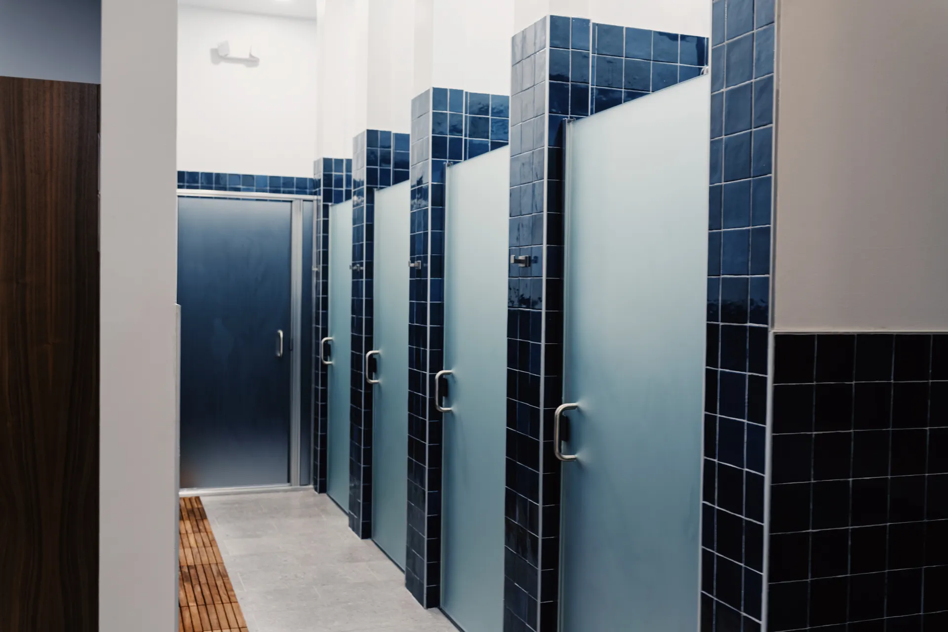 The men's locker room at THIS Gym — navy tile, grooming stations, and private showers — image 3 of 3